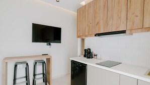A modern kitchen with white cabinets, a black dishwasher, a coffee maker, and two bar stools. - Aelia Prime Experience 3 (Kos)