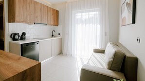 A modern kitchen with wooden cabinets, a dishwasher, and a coffee maker. There is a dining table and a sofa in the living area. - Aelia Prime Experience 3 (Kos)