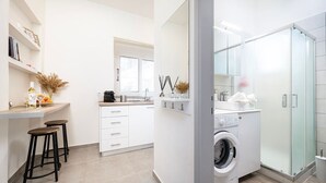 A modern kitchen with white cabinets, a built-in oven, and a countertop with bar stools. - Coastal Elegance Suite 1Min to the Beach (Kos)