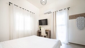 A bedroom with a large bed, a desk with a chair, a TV mounted on the wall, and a unique geometric wall art piece. - Coastal Elegance Suite 1Min to the Beach (Kos)