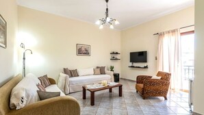 A living room with a sofa, armchair, coffee table, and a TV. - Beachside Retreat Steps to Kos (Kos)