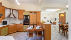 A modern kitchen with wooden cabinets, a dining area with a table set for four, and a living area with a sofa and a TV. - Beachside Retreat Steps to Kos (Kos)