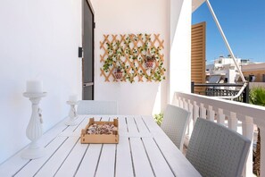 Een witte houten tafel met een snackdoos, twee witte kandelaars en een sprietmuur met hangende plantenbakken op een balkon.