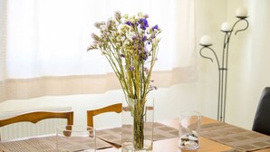 A dining table with a vase of flowers, a glass of stones, and a candle holder. - Beachside Retreat Steps to Kos (Kos)