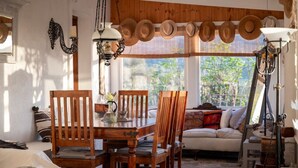 A cozy room with a wooden dining table, chairs, and a sofa. There are hats hanging on the wall, a lamp, and a window with a view of greenery. - Paradiso Vintage Villa: Traditional 1944 Gem (Pili)