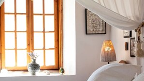 A bedroom with a large bed, a window with a wooden frame, and a bedside lamp. - Paradiso Vintage Villa: Traditional 1944 Gem (Pili)