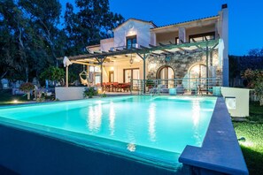 Et moderne hus med swimmingpool, udendørs møbler og en facade i sten.