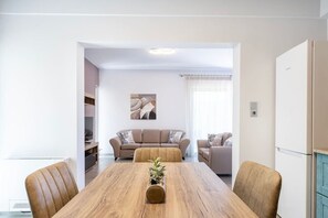 A modern living room with a wooden dining table, two sofas, and a kitchen area with a refrigerator.