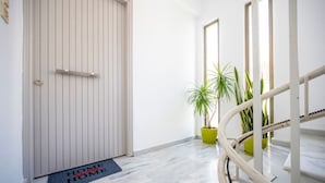 Un couloir avec une porte fermée, un paillasson et des plantes en pot.