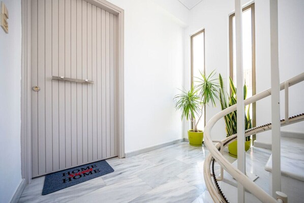 Un couloir avec une porte fermée, un paillasson et des plantes en pot.