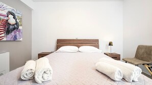 Une chambre d’hôtel moderne avec un grand lit, une tête de lit en bois, une table de chevet avec une lampe, une chaise et un tableau au mur.