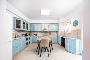 A kitchen with light blue cabinets, a marble countertop, and a dining table with chairs.