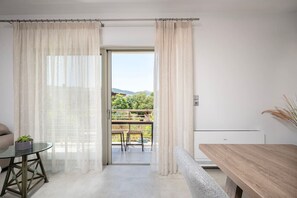 A room with a glass door leading to a balcony, a round table, a bench, and a radiator.