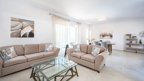 Un salon moderne avec deux canapés beige, une table basse en verre et un coin repas comprenant une table et des chaises.
