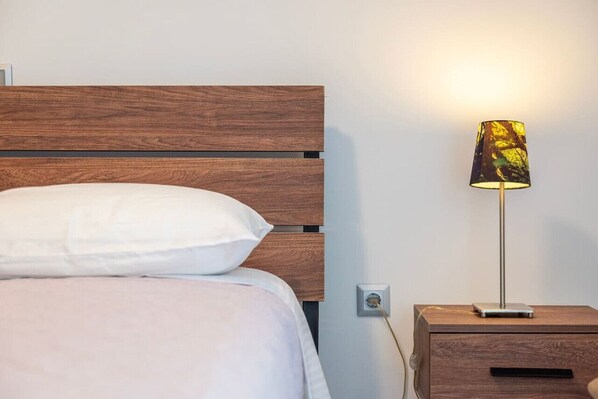 A bed with a wooden headboard, a white pillow, and a bedside table with a lamp.