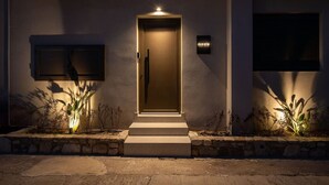 A modern house with a lit entrance, a small garden, and a signboard. - Beach Luxury Homes : Nicole (Kos)