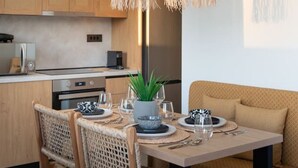 A modern kitchen with wooden cabinets, a dining table set for four, and two hanging woven light fixtures. - Beach Luxury Homes : Nicole (Kos)