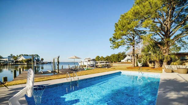 En rektangulär swimmingpool med ett klart, blått vatten, omgiven av en terrass med solstolar och ett litet bord.