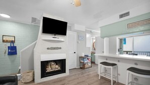Una sala de estar moderna con chimenea, un televisor montado encima y una zona de bar con taburetes.