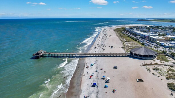 Vista aérea de una playa con un muelle, sombrillas y un pabellón.