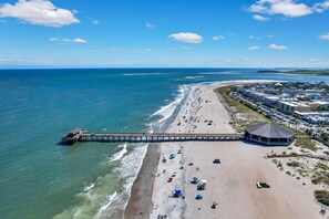 An aerial view of a beach with a pier, beach umbrellas, and a gazebo.