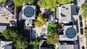 An aerial view of a hotel complex with multiple buildings, each featuring a logo with the name 'ROYCE' and 'Spring'. There are outdoor seating areas with tables and chairs, surrounded by trees.