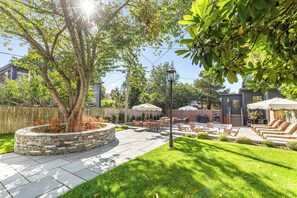 A backyard with a stone planter, patio furniture, and a barbecue area.