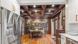 A modern kitchen with wooden flooring, stainless steel appliances, a dining area with a round table, and a chandelier.