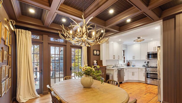 A spacious dining area with a large wooden table, surrounded by chairs, and a chandelier.