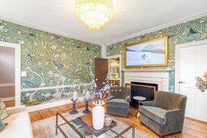 A living room with a fireplace, a large painting, and a chandelier.