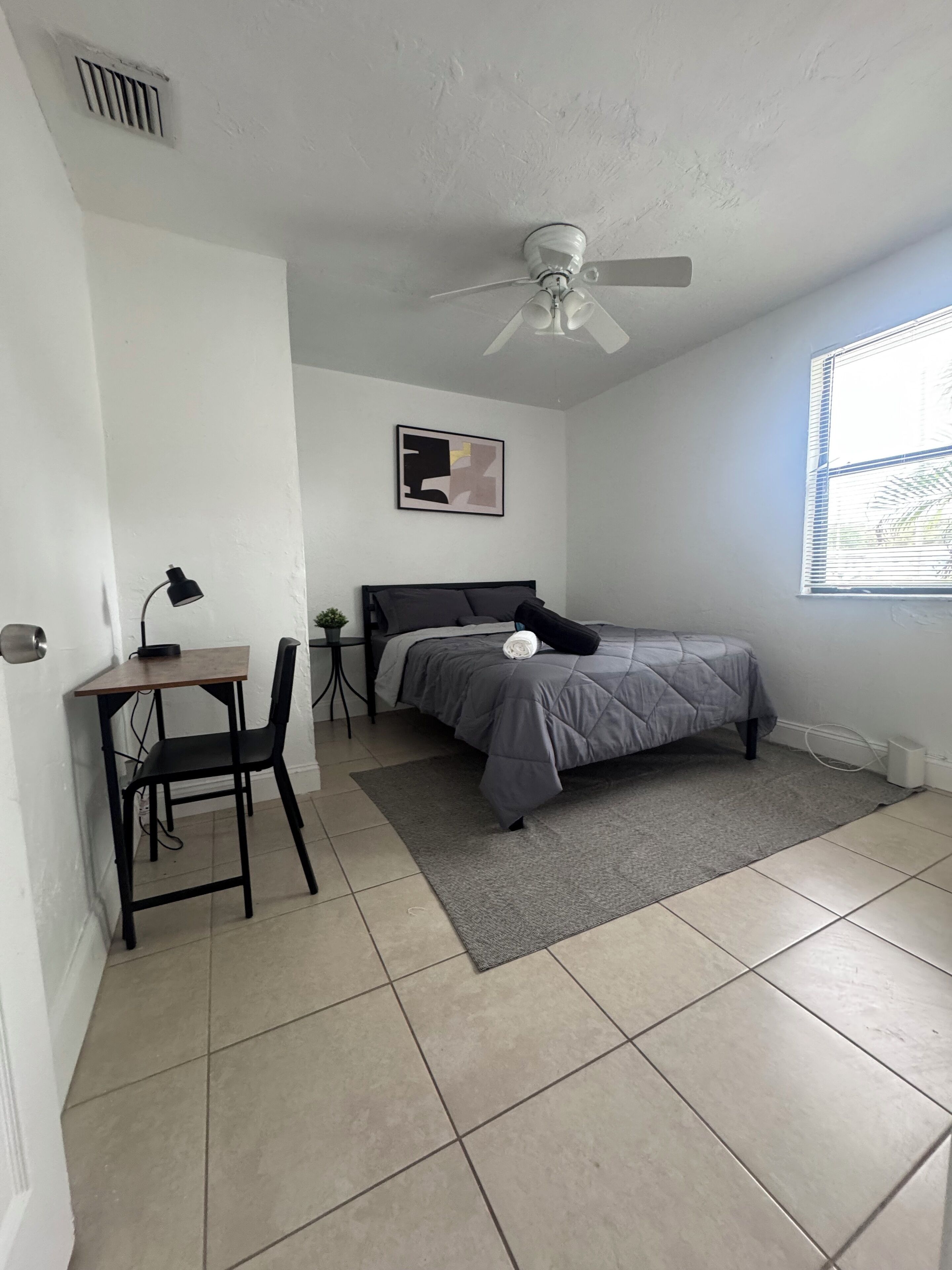 A bedroom with a bed, desk, chair, and a ceiling fan.