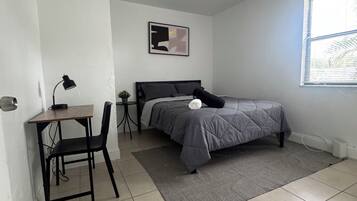 A bedroom with a bed, desk, chair, and a ceiling fan.