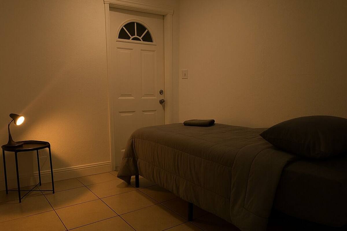 Een slaapkamer met een bed, nachtkastje, deur en een plafondlamp.