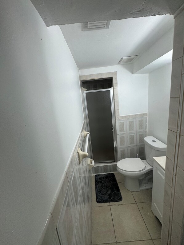 Un baño estrecho con inodoro, cabina de ducha y lavamanos pequeño.
