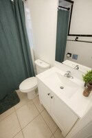 Een badkamer met een wit wastafelmeubel, toilet en douchegordijn.