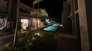 Ein modernes Hotel mit Swimmingpool, Palmen und einem gut beleuchteten Eingangsbereich.