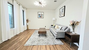 Ein modernes Wohnzimmer mit grauem Sofa, Holztisch und gemustertem Teppich.