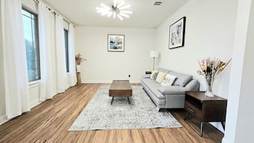 Ein modernes Wohnzimmer mit grauem Sofa, Holztisch und gemustertem Teppich.