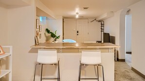 A modern kitchen with a central island, two white bar stools, a potted plant, and a white door.