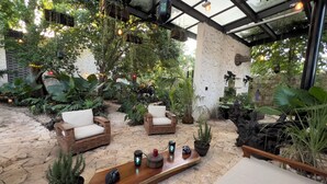 A covered outdoor seating area with wicker furniture, potted plants, and a wooden table with decorative items. - Casa Shakti a paradise in the city (Mérida)