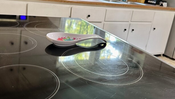Een keuken met een zwarte inductiekookplaat, een magnetron en een raam met uitzicht op bomen.