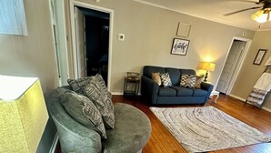 Een woonkamer met een grijze fauteuil, een blauwe bank, een vloerkleed met patroon en een houten vloer.