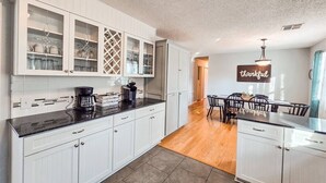 Una cocina con gabinetes blancos, una cafetera y un comedor con mesa y sillas.