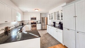 Una cocina con armarios blancos, encimera negra, electrodomésticos de acero inoxidable y suelo de madera.