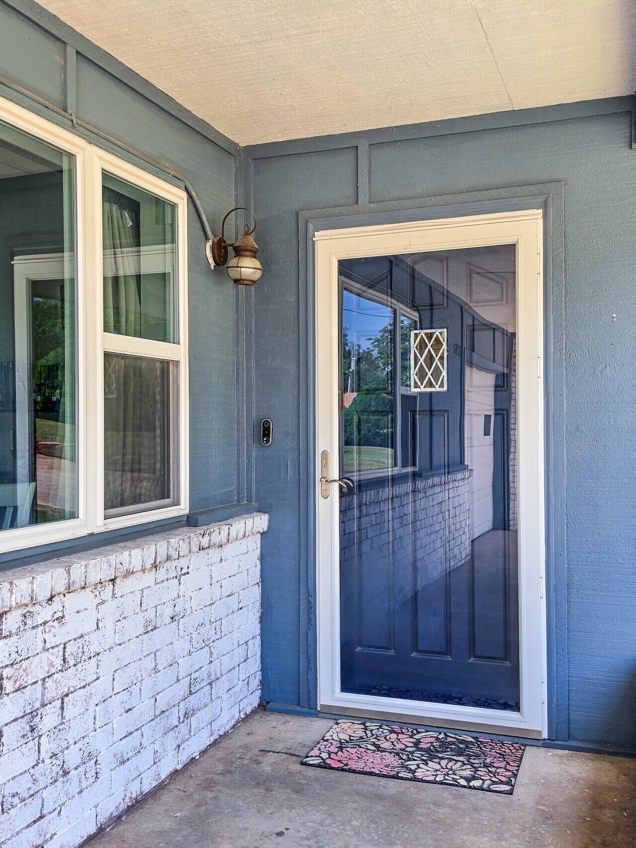 A house with a dark blue exterior, a white brick base, a front door with a glass panel, and a small porch area.