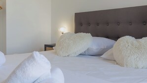 A neatly made bed with white linens and fluffy pillows, a bedside lamp, and a dark headboard.