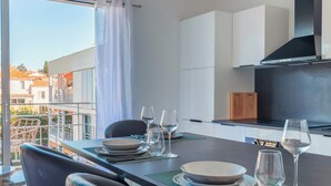 A modern dining area with a balcony view, a kitchen with a black range hood, and a dining table set with plates and wine glasses.
