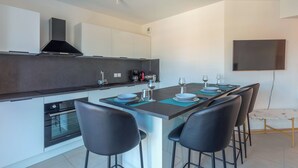 A modern kitchen with a central island, bar stools, and a flat-screen TV mounted on the wall.