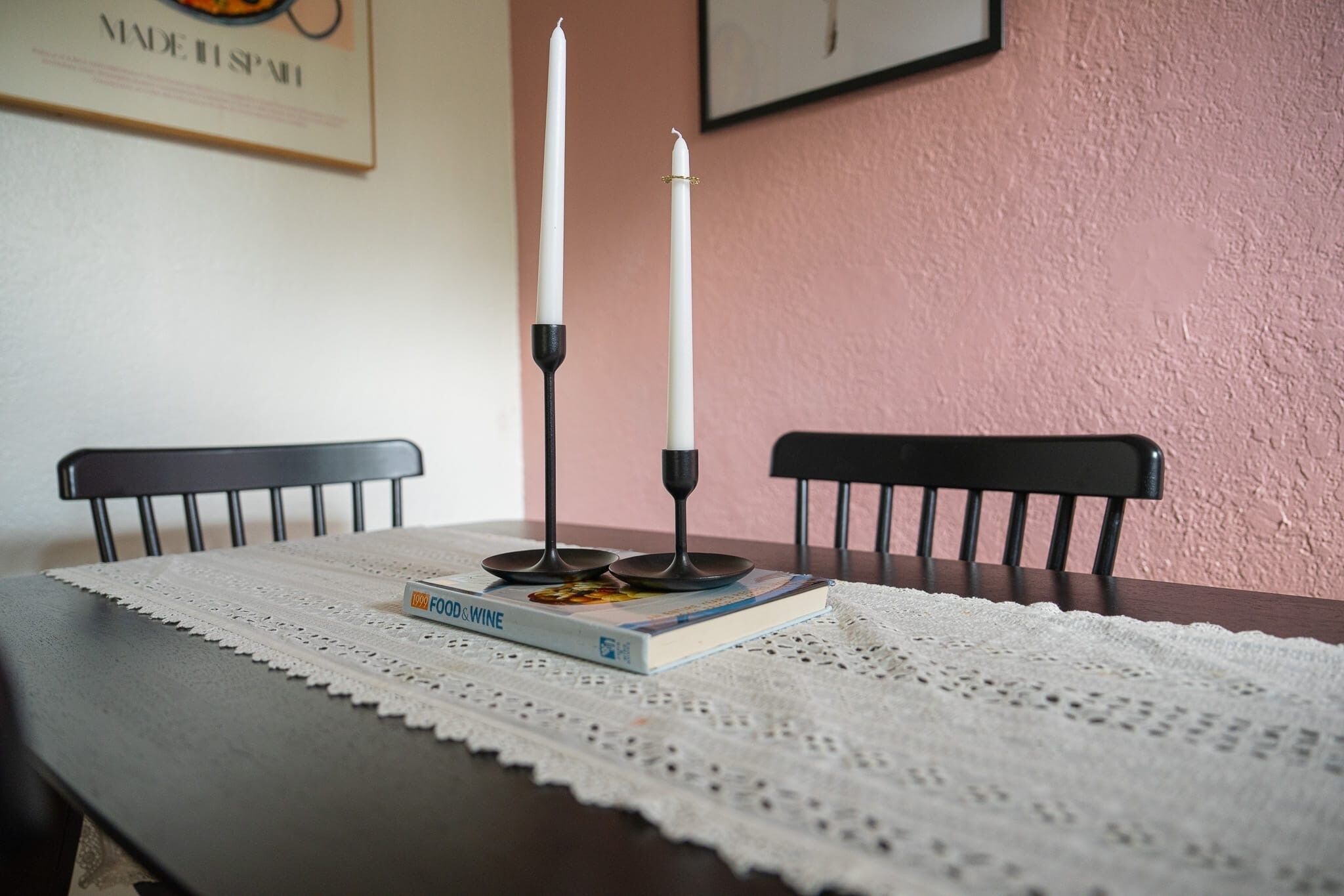 Een tafel met een kant kleed, een boek met de titel 'FOOD & WINE' en twee kaarsen in zwarte kandelaars.