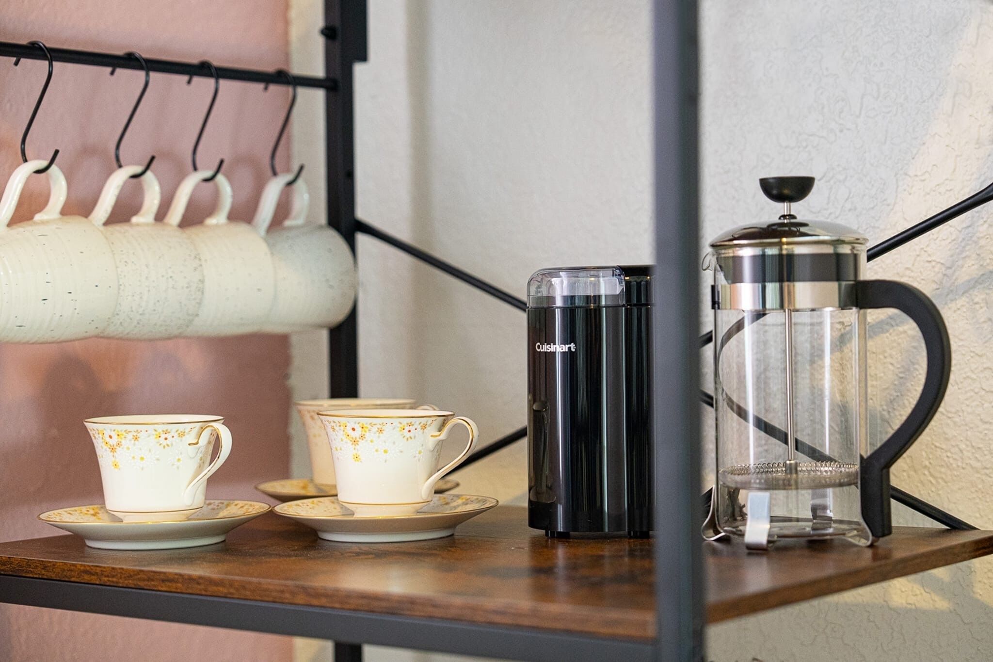 A coffee setup with a coffee press, two cups, and a saucer on a shelf.